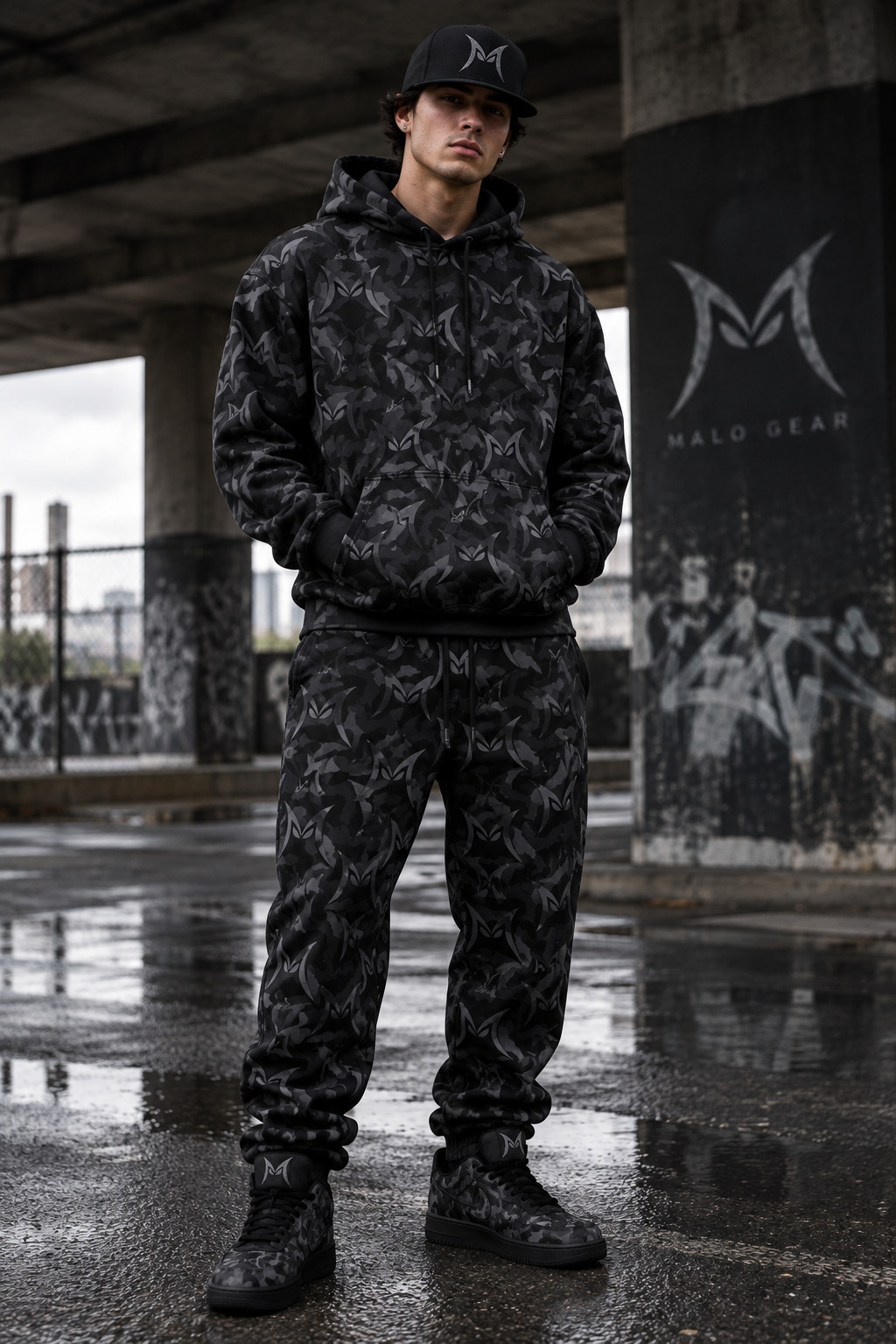 Model wearing the MALO M camo all-over print hoodie, sweatpants, and sneakers, with the M logo on the hat